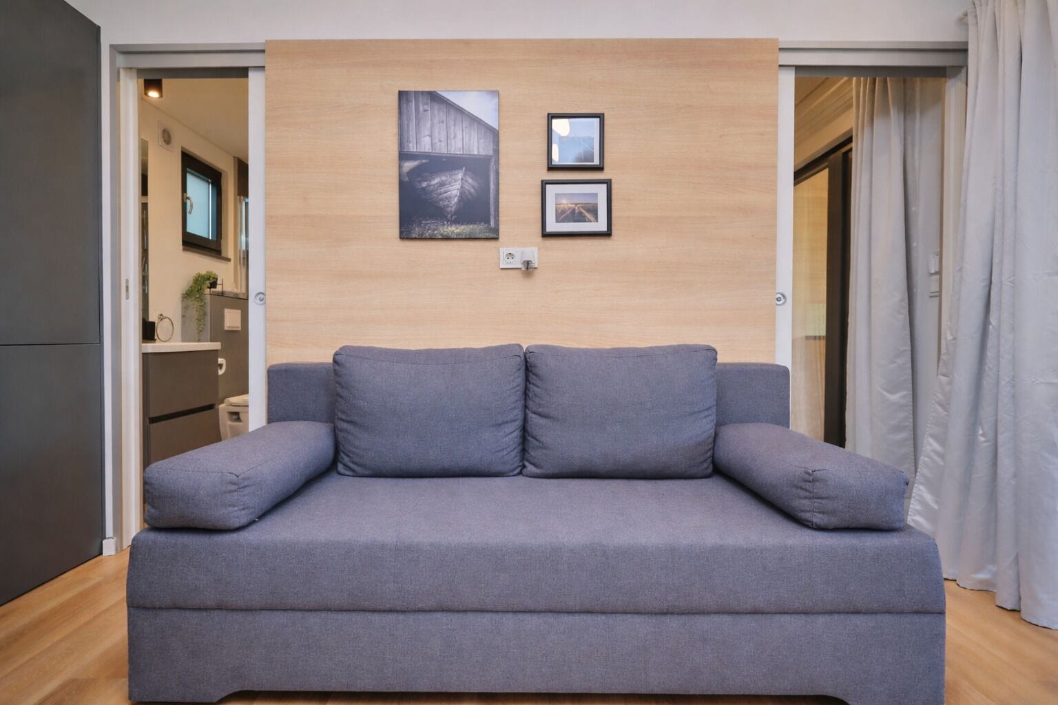 A grey sofa in a room with wooden walls, a door, and a window.