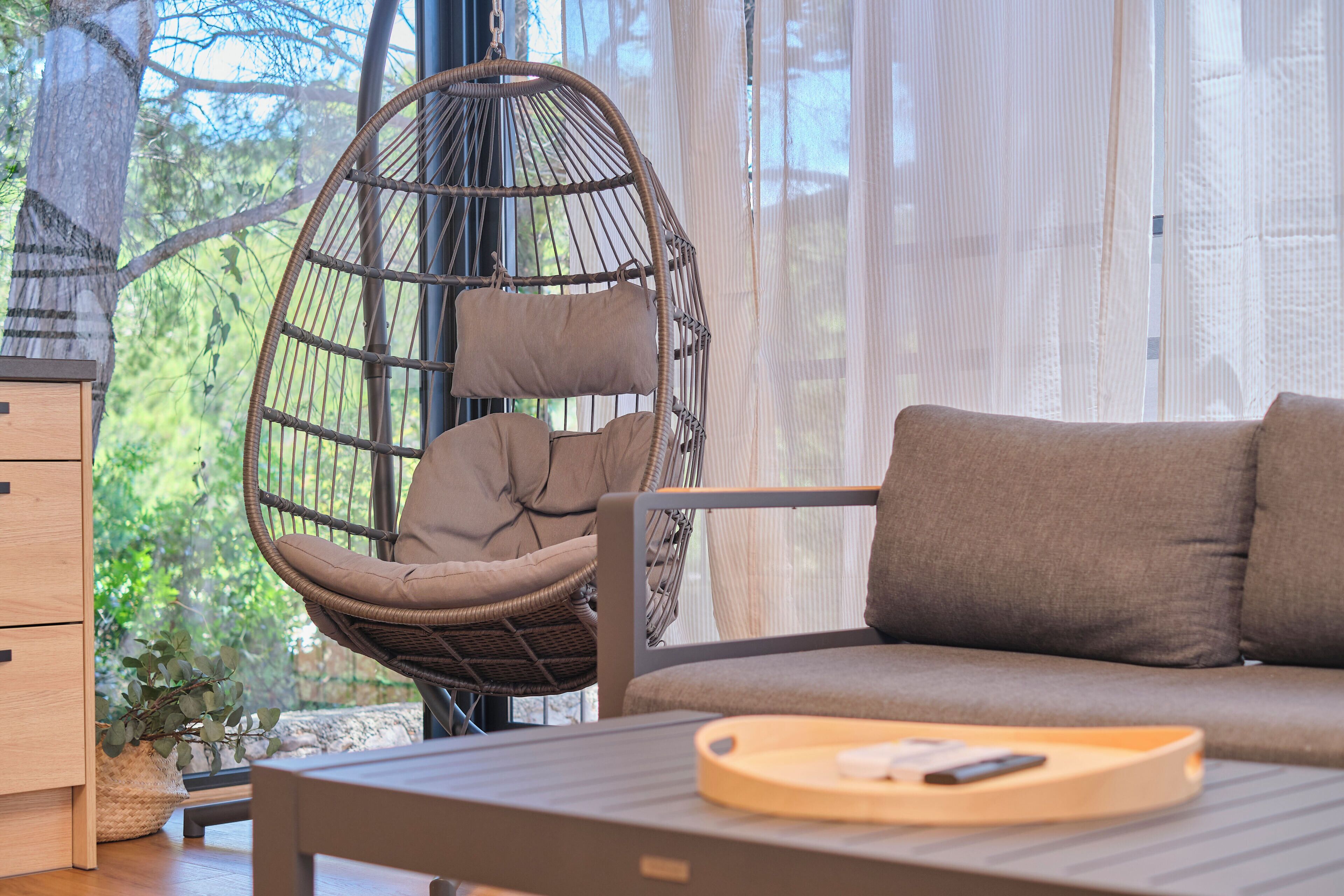 Een moderne woonkamer met een hangstoel, een bank en een houten tafel met dienblad.