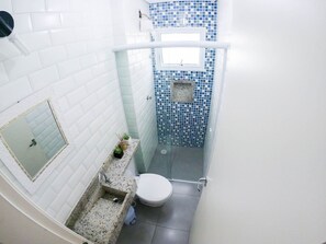 A small bathroom with a toilet, sink, mirror, and a shower area with blue mosaic tiles. - Condomínio Veneza (Ubatuba)