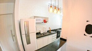 A compact kitchen with white cabinets, a black countertop, a microwave, and a gas stove. - Condomínio Veneza (Ubatuba)