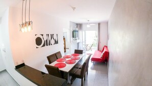 A modern dining area with a long table, chairs, and a red sofa. - Condomínio Veneza (Ubatuba)