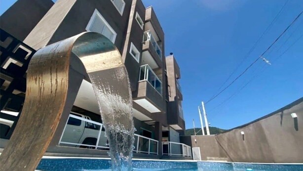 A modern building with a unique angular design, a swimming pool, and a large metal sculpture. - Condomínio Veneza (Ubatuba)