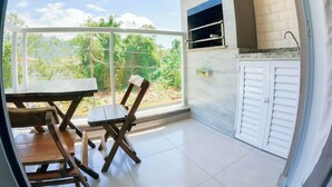 A balcony with a table and chairs, a brick wall, and a window overlooking greenery. - Condomínio Veneza (Ubatuba)
