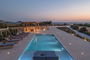A poolside area with lounge chairs, a pergola, and a view of the sea at dusk. - Villa Armelina New Luxury Beachfront Villa with Private Pool (Naxos)