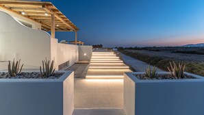 A modern outdoor pathway leading to a building with a wooden pergola and a view of the sea.