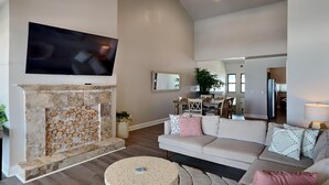 Un salon moderne avec une cheminée en pierre, un téléviseur à écran plat, un canapé agrémenté de coussins à motifs et, au fond, un coin repas.