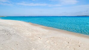 Une plage avec une eau d’un bleu limpide et un rivage sablonneux.