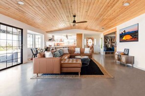 A spacious living area with a large sectional sofa, a dining table, and a kitchen in the background.