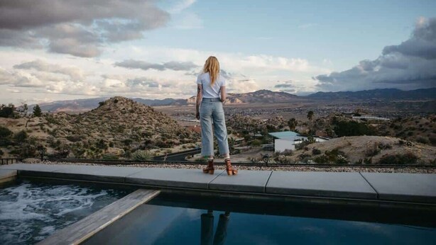 A person standing by a pool with a view of a desert landscape and mountains.