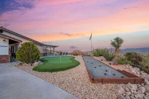 A house with a number '56969' on the side, a putting green, a croquet field, and a flagpole with an American flag.