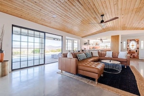 A spacious living area with a large sectional sofa, a round coffee table, and a ceiling fan.