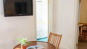 A dining area with a round wooden table, four wooden chairs, a potted plant, and a flat-screen TV mounted on the wall. - Historic 2BR Nantucket Cottage | Walk to Downtown (Nantucket)