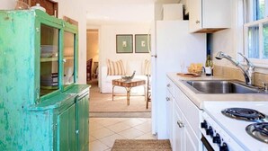 A kitchen with a stove, sink, and cabinets. There is a dining area with a table and chairs in the background. - Historic 2BR Nantucket Cottage | Walk to Downtown (Nantucket)