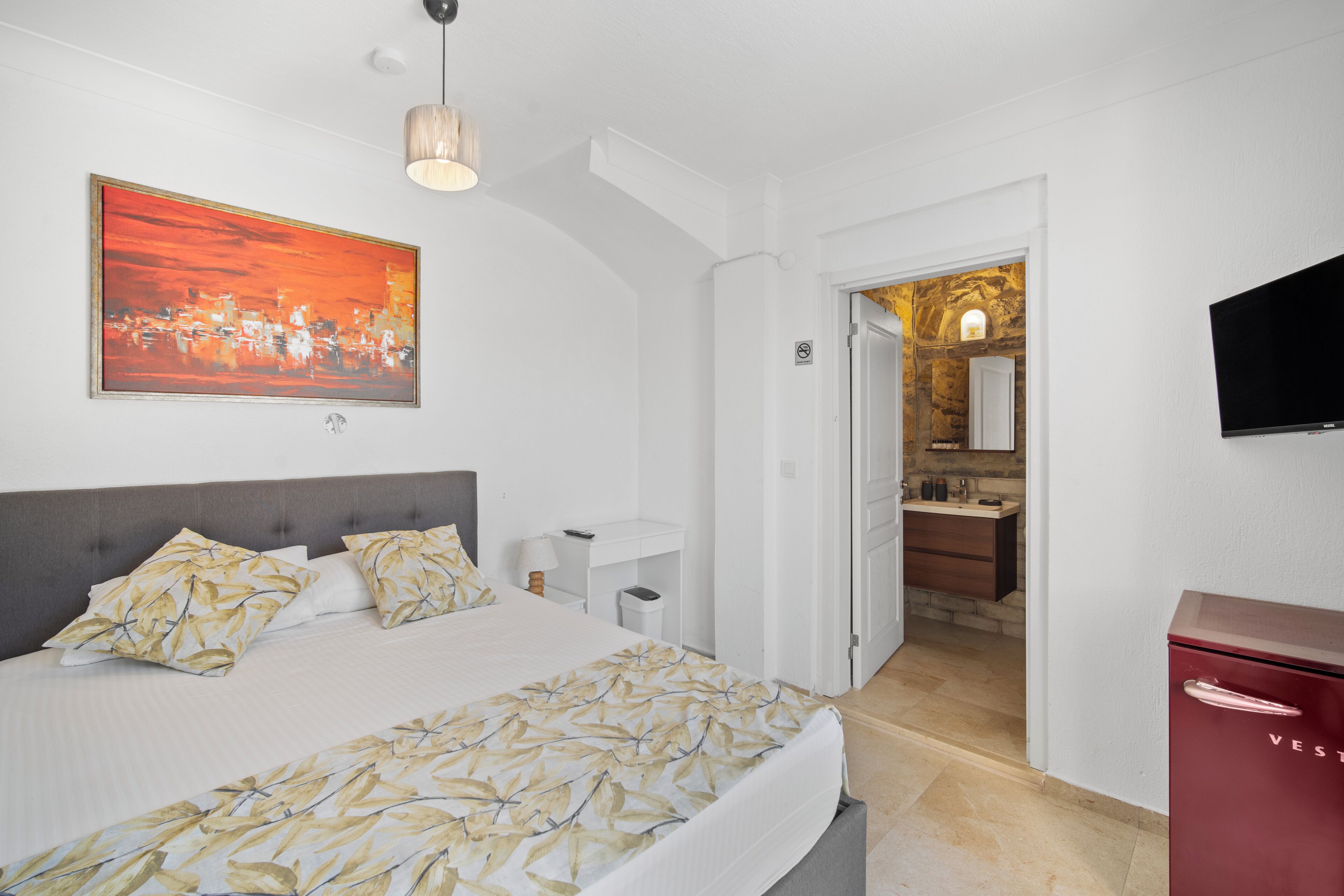 A hotel room with a bed, a painting, a television, and a red cabinet.