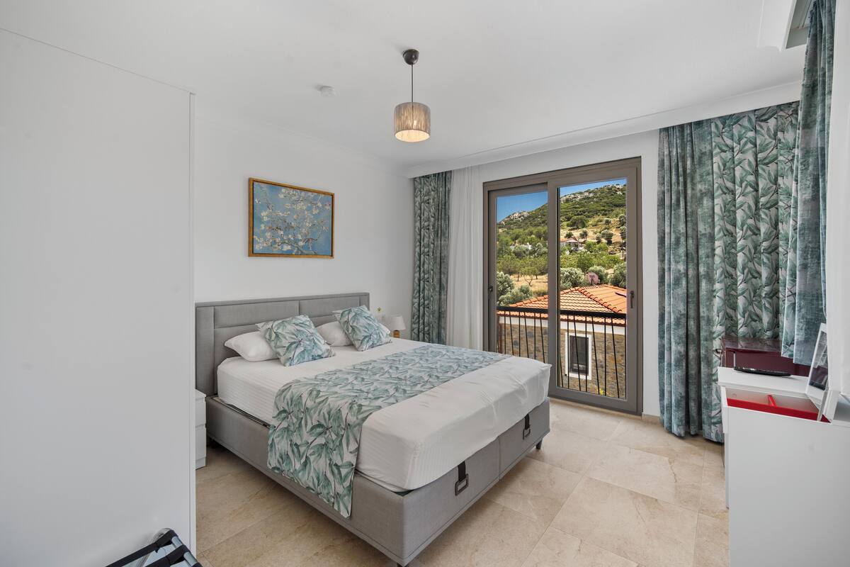 A bedroom with a bed, a desk, a chair, a window with curtains, and a painting on the wall.