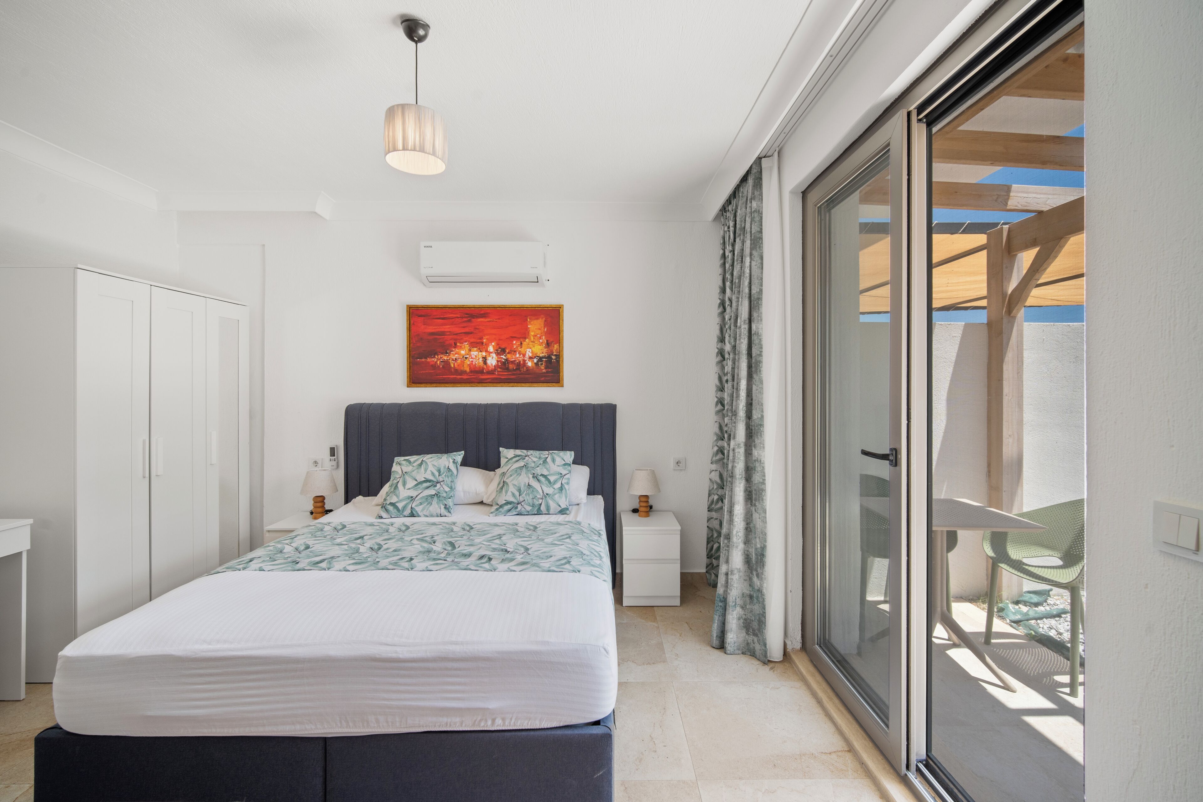 A bedroom with a bed, nightstands, a painting, and a sliding glass door to a balcony.