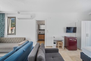 Una sala moderna con un sofá, un televisor, un escritorio pequeño y un refrigerador.