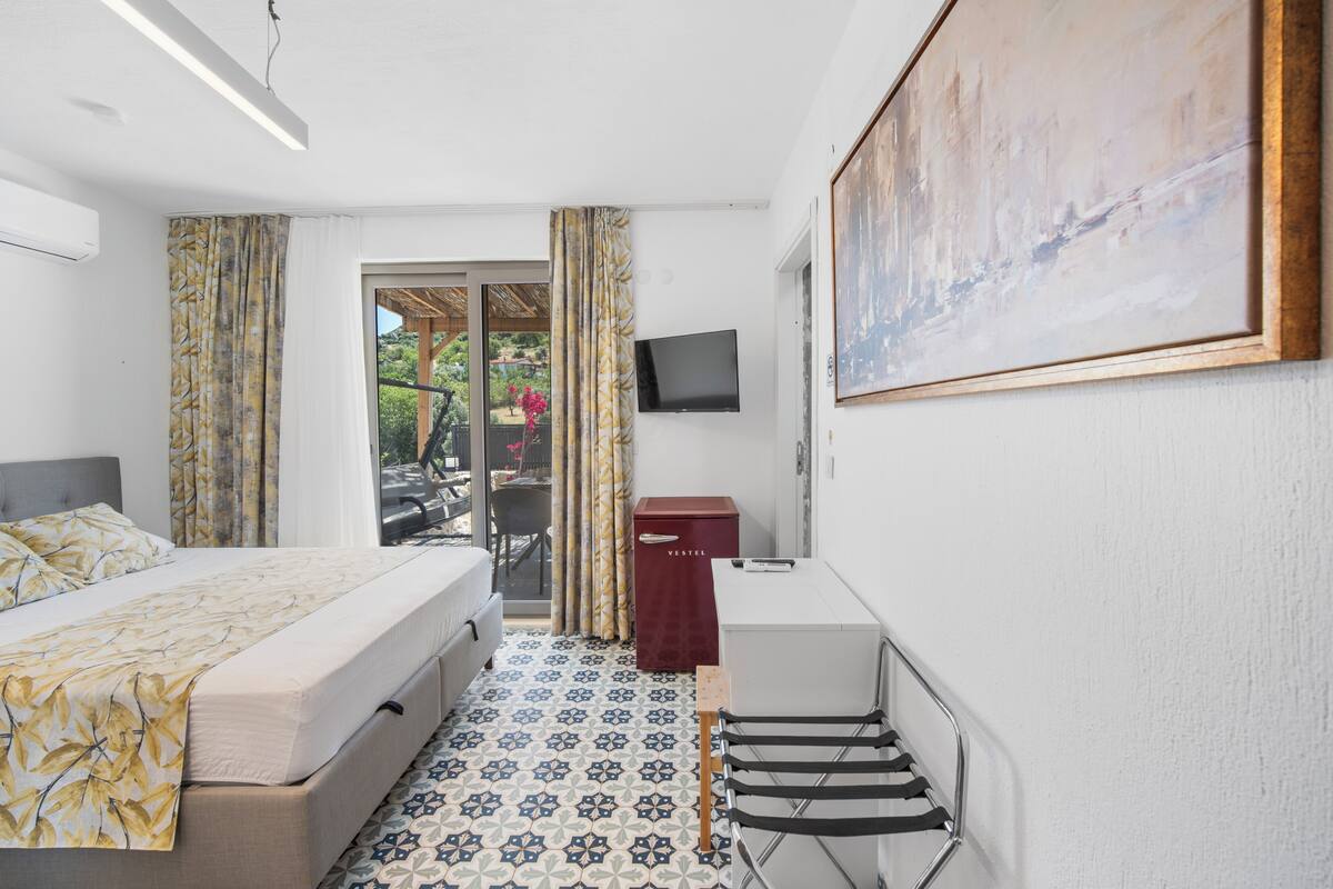 A hotel room with a bed, a desk, a TV, and a painting on the wall.