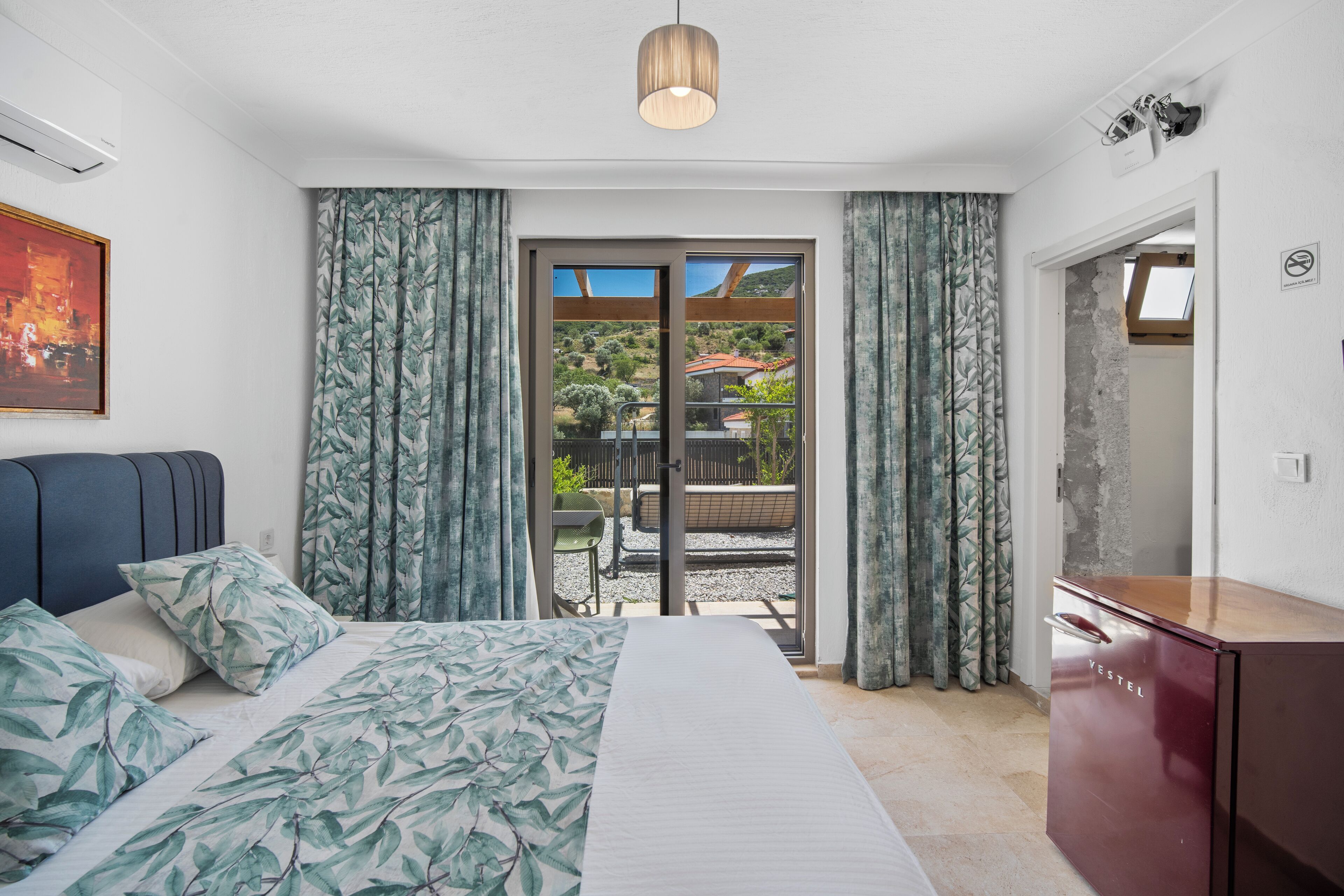 Quarto com cama, cortinas, escrivaninha e vista para o exterior.