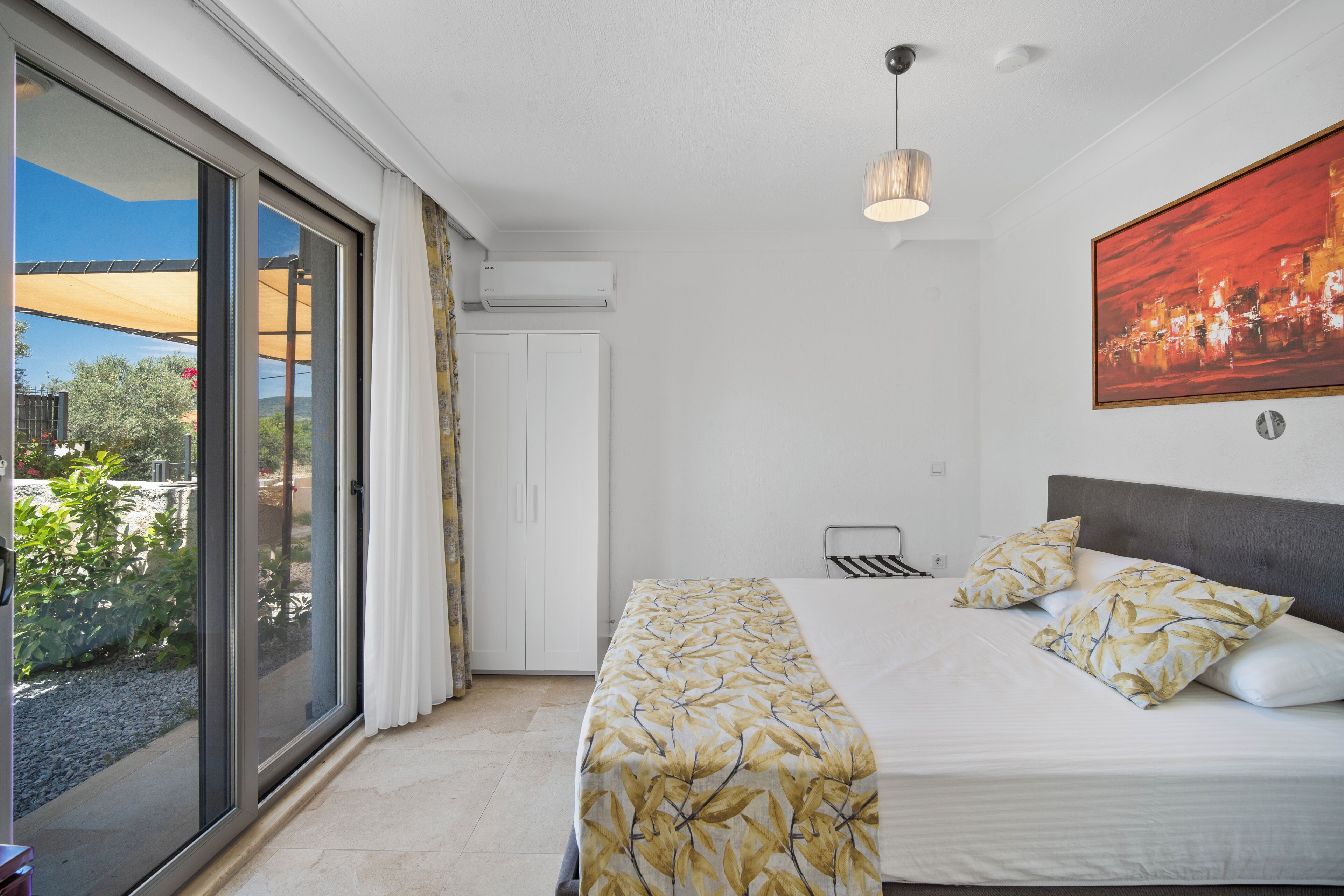 Une chambre à coucher avec un lit, un luminaire au plafond, une fenêtre avec des rideaux et un tableau accroché au mur.