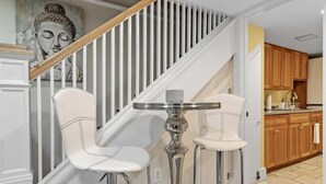 Een trap met witte leuningen en een houten handrail, die leidt naar een keuken met houten kastjes en een roestvrijstalen spoelbak.