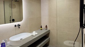 Ein modernes Badezimmer mit einem weißen Waschbecken, zwei Seifenspender, einem Handtuch und einer Dusche mit Glastür.