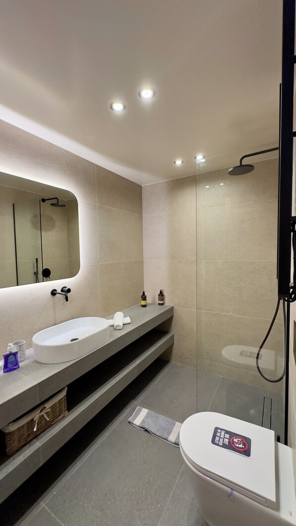 A modern bathroom with a white sink, two bottles of soap, a towel, and a shower with a glass door.