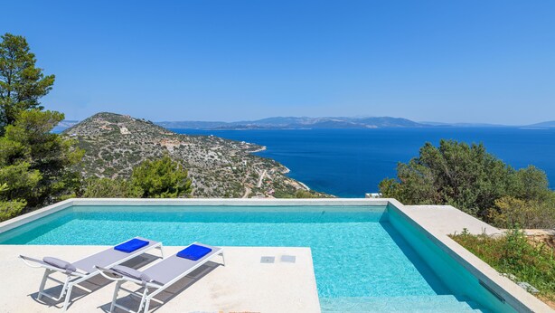 Ein Pool mit zwei Liegestühlen und Blick auf das Meer und die Berge.