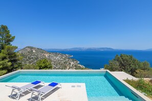 A pool with two lounge chairs and a view of the sea and mountains.