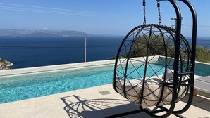 Ein Hängesessel am Pool mit Blick auf Meer und Berge.