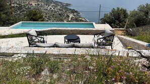 Ein Pool mit Liegestühlen und einem Tisch mit Blick auf eine malerische Seenlandschaft und ferne Berge.