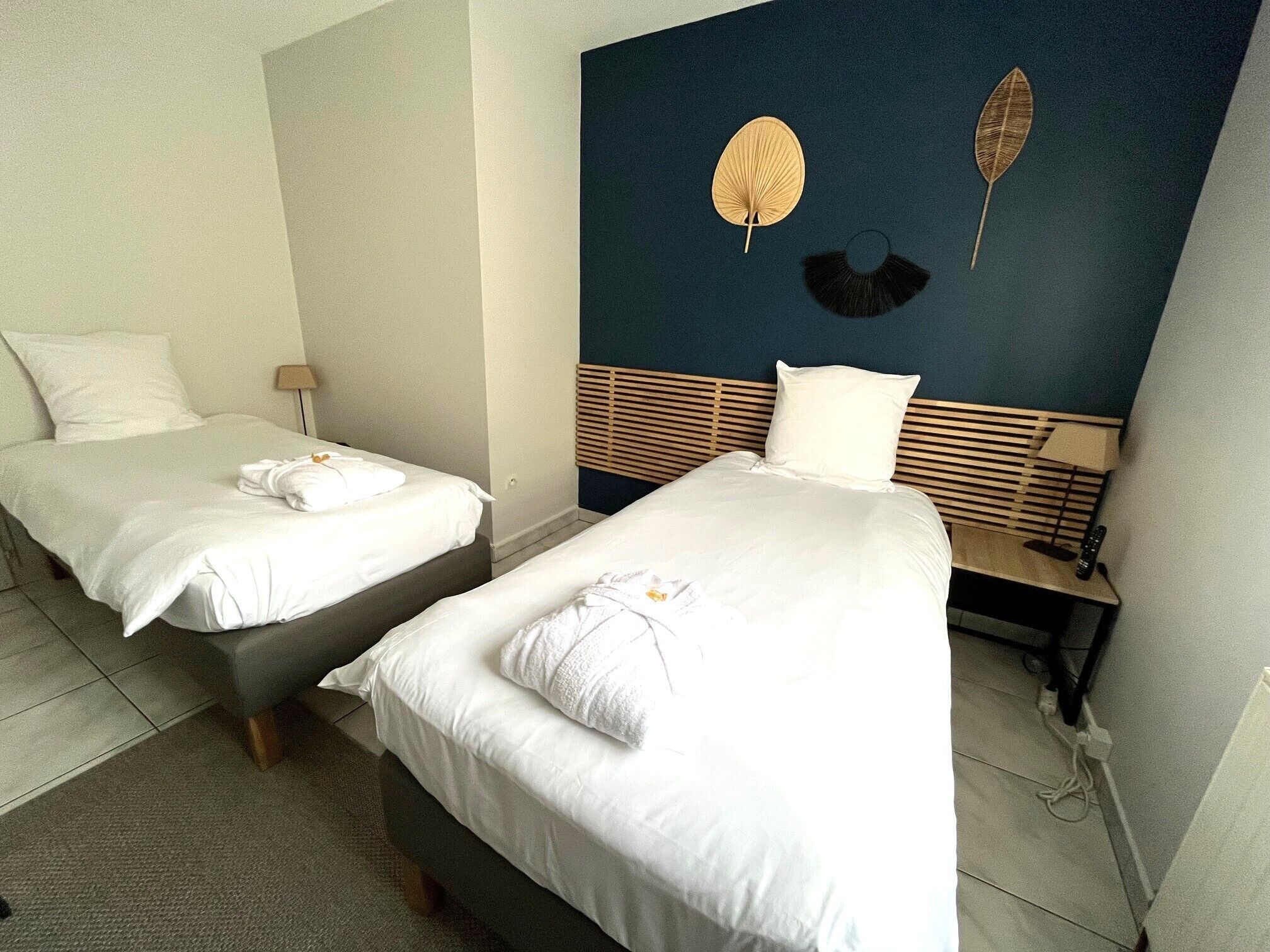 A hotel room with two beds, each with white linens and pillows, a wooden headboard, and a wall-mounted lamp.