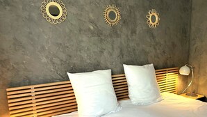 Ein ordentlich bezogenes Bett mit weißen Leinen und zwei Kissen, ein hölzernes Kopfteil sowie drei an der Wand befestigte, sternförmige Spiegel.