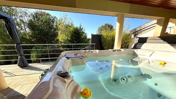 Ein Whirlpool mit einer Schwimmenten, umgeben von einer Holzterrasse und einem Metallgeländer.