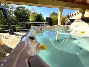 A hot tub with a duck float, surrounded by a wooden deck and a metal railing. - "La Loupiote - Gîte Éclairé" Maison de Village Proche Nancy Avec Grand Jacuzzi ! (Lupcourt)