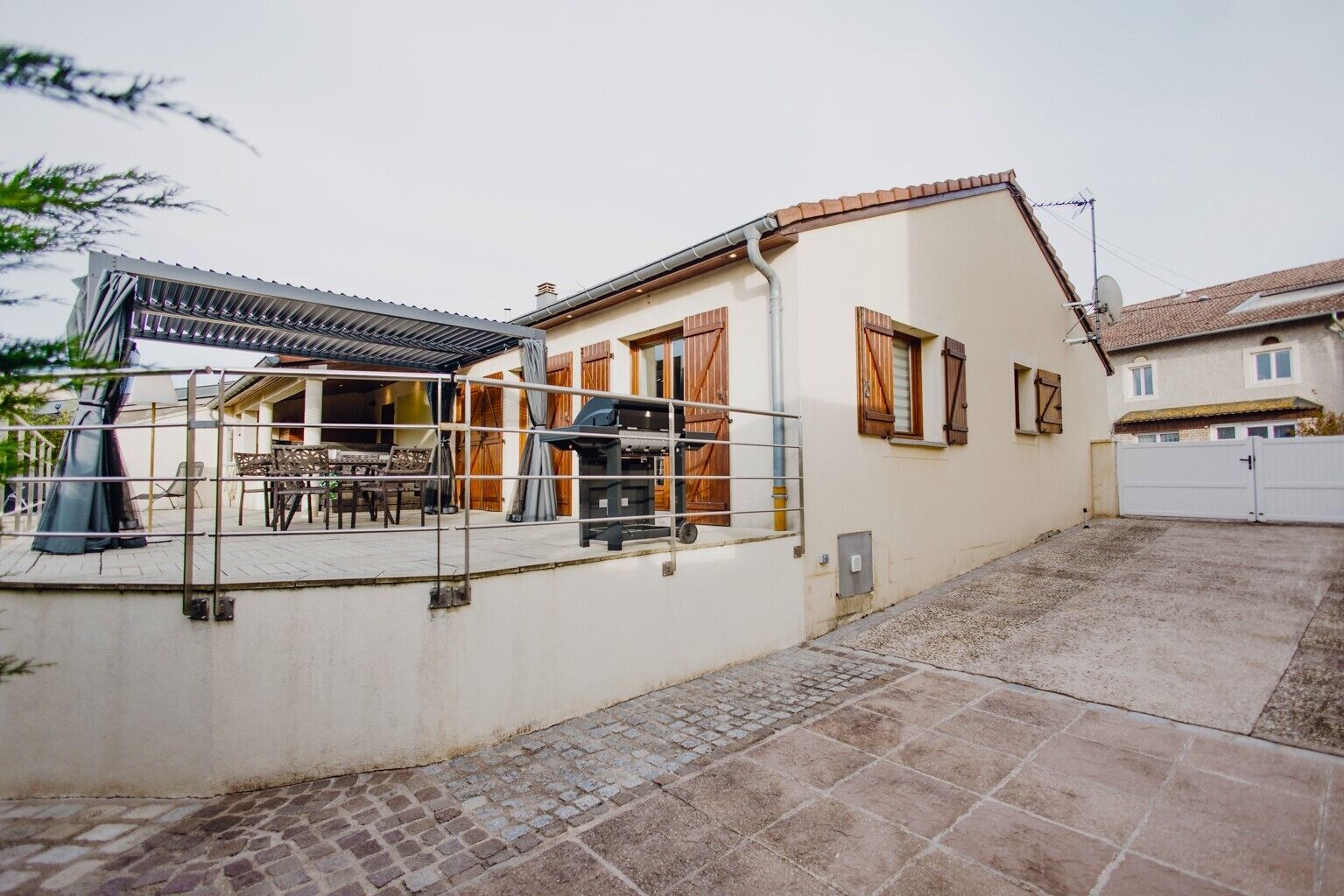 Een huis met een terras, een barbecue en een hekpoort bij de oprit.