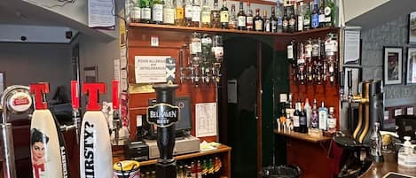Zona de bar con mostrador, varias botellas, un reloj y un cartel que indica alérgenos e intolerancias alimentarias.