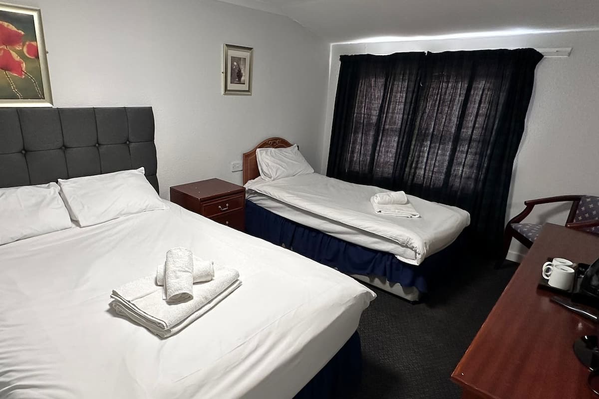 A hotel room with two beds, a wooden nightstand, a desk with a chair, and a window with curtains.