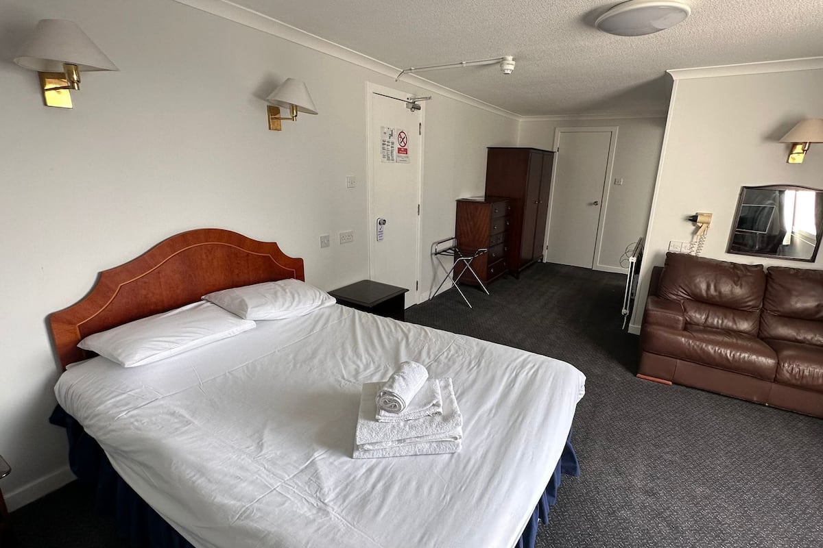A hotel room with a bed, a brown leather sofa, a small table, and a mirror.