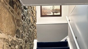 Una escalera con alfombra azul oscuro, una pared de piedra a un lado y un marco de cuadro en la pared de arriba.