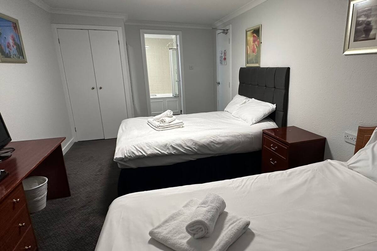 A hotel room with two beds, a desk, a chair, a window, and a door.