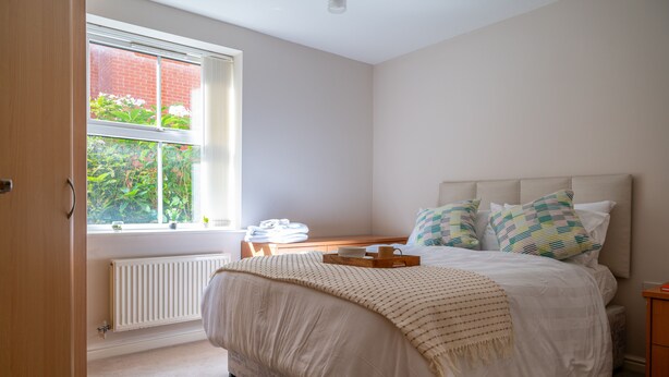 A bedroom with a bed, a window, a radiator, and a wooden nightstand. - Spacious Apartment, Near to NEC and City Centre.  (Solihull)