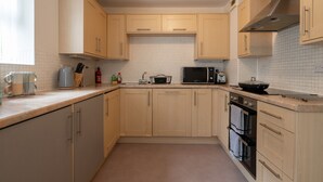 A kitchen with light wooden cabinets, a microwave, a toaster, and a kettle. - Spacious Apartment, Near to NEC and City Centre.  (Solihull)