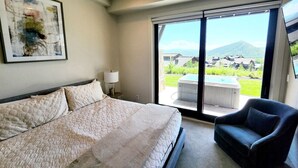 Habitación de hotel con una cama grande, una silla, un escritorio y vistas a un paisaje montañoso a través de una puerta corredera.