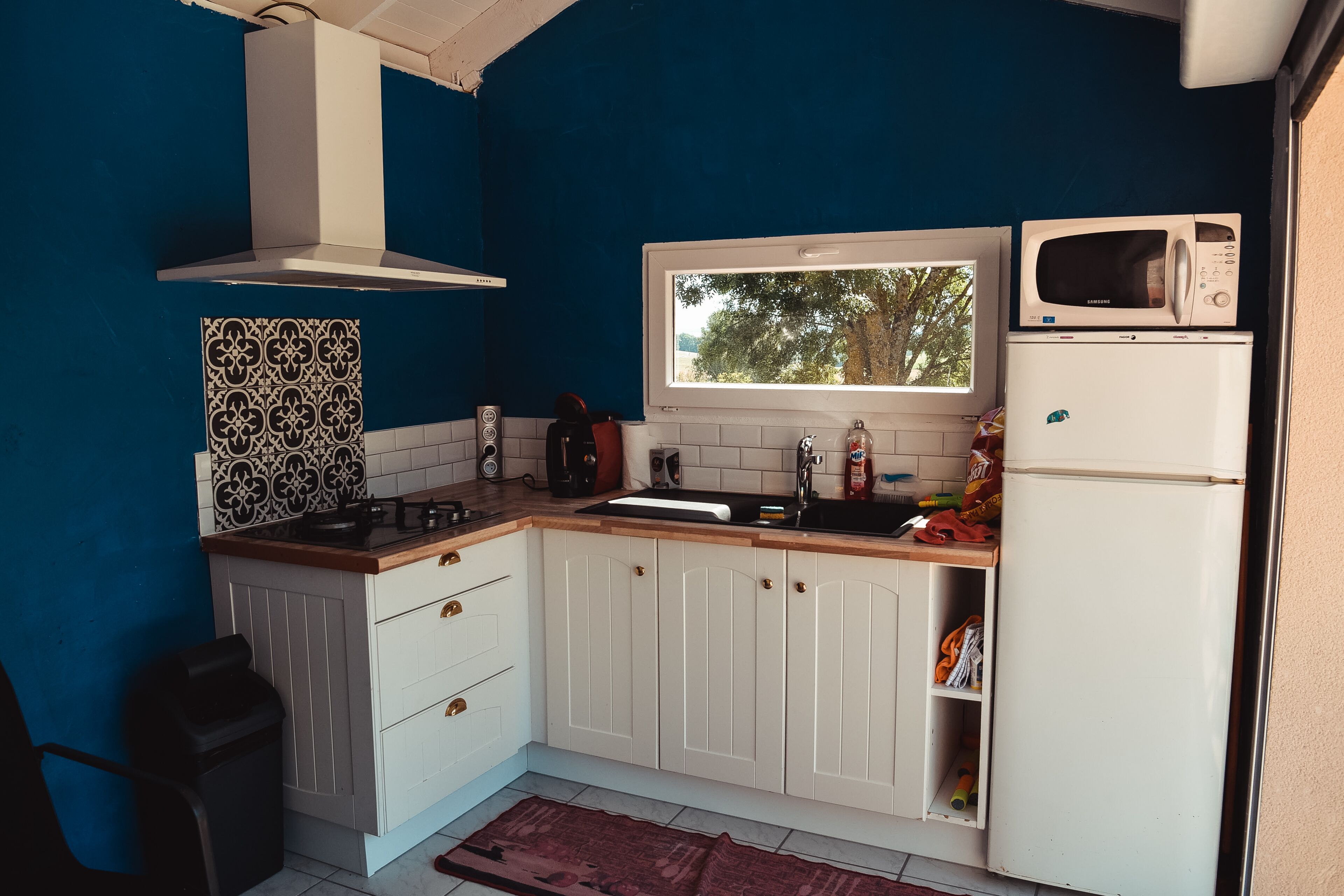 A compact kitchen with white cabinets, a microwave, a sink, and a window.