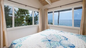 A bedroom with a large bed, two windows, and a view of the sea.