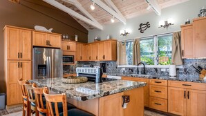 A kitchen with wooden cabinets, a stainless steel refrigerator, a granite countertop, and a window with curtains.