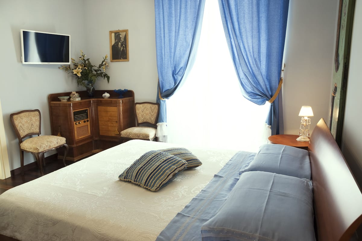 A neatly arranged bedroom with a large bed, a television mounted on the wall, a dresser, and a chair.
