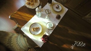 Une table à manger dressée avec des assiettes, des tasses et une théière, ce qui laisse supposer qu’un petit-déjeuner ou un service à thé va être servi.