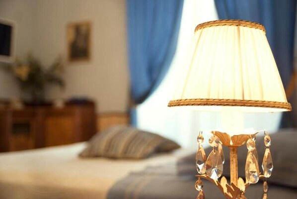 Una lámpara con pantalla plisada sobre una mesita de noche en una habitación de hotel.